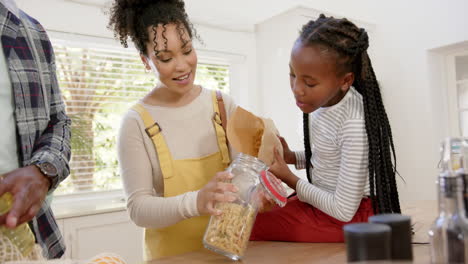 happy african american parents and daughter pouring pasta into jar at home, slow motion