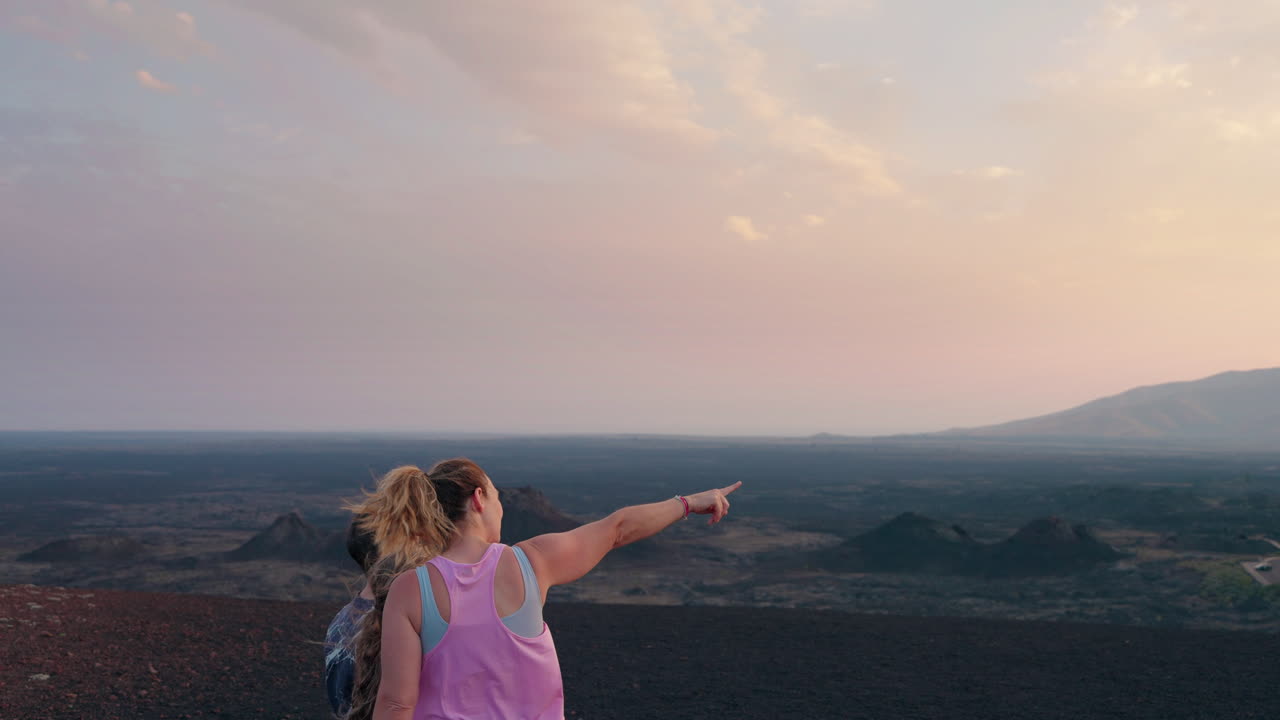 Two people observing a vast volcanic landscape at sunrise or sunset