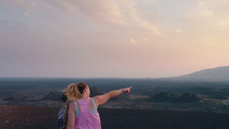 two people observing a vast volcanic landscape at sunrise or sunset