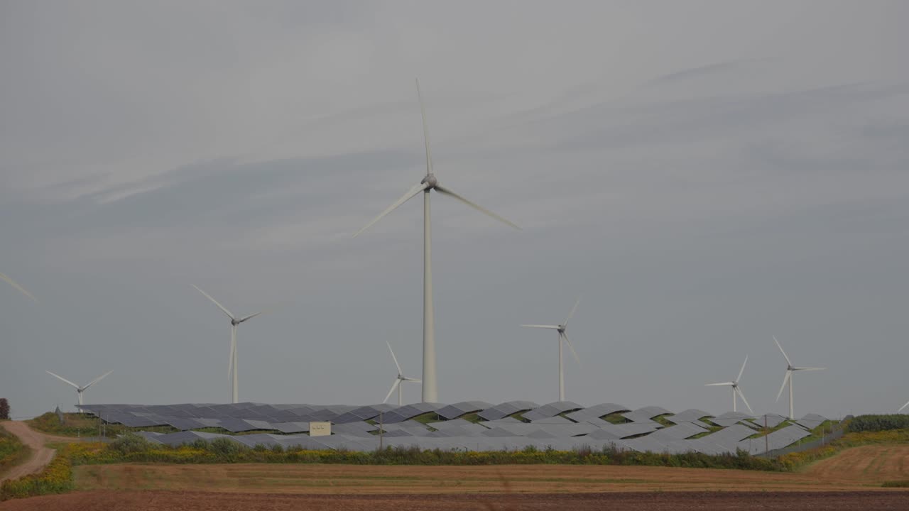 Wide view of wind turbines and solar panels in a rural field under a cloudy sky, symbolizing clean and sustainable energy production