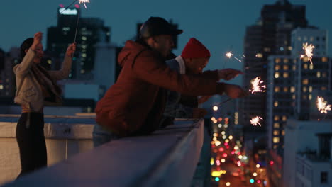 Fröhliche-Freunde-Halten-Wunderkerzen-In-Der-Hand-Und-Feiern-Silvester-Auf-Dem-Dach-Bei-Sonnenuntergang-Und-Haben-Spaß-Daran,-Die-Feiertagsfeier-Zu-Genießen