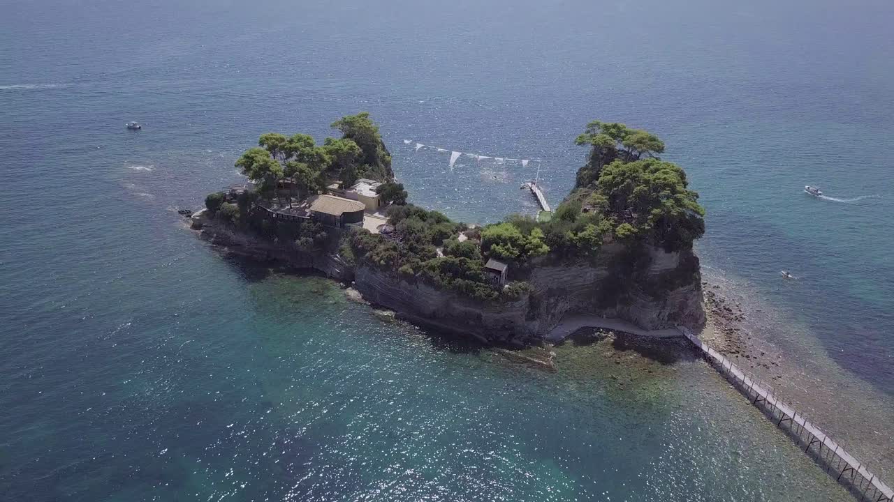 imágenes de drones de rotación lenta hacia adentro de una pequeña isla rocosa frente a la costa de zakynthos, grecia, con un clima claro y soleado y mares azules
