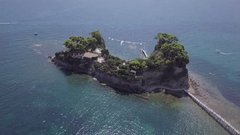 Imágenes-De-Drones-De-Rotación-Lenta-Hacia-Adentro-De-Una-Pequeña-Isla-Rocosa-Frente-A-La-Costa-De-Zakynthos,-Grecia,-Con-Un-Clima-Claro-Y-Soleado-Y-Mares-Azules