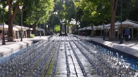 Defocused-background:-Low-key-water-fountains-in-sun-dappled-city-park