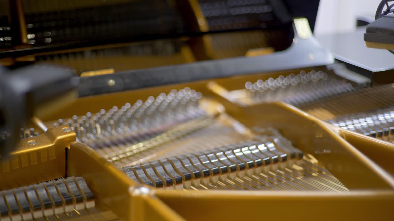 Hammers of an open concert grand piano moving during a recording session in a studio with condenser microphones at the corner of the frame