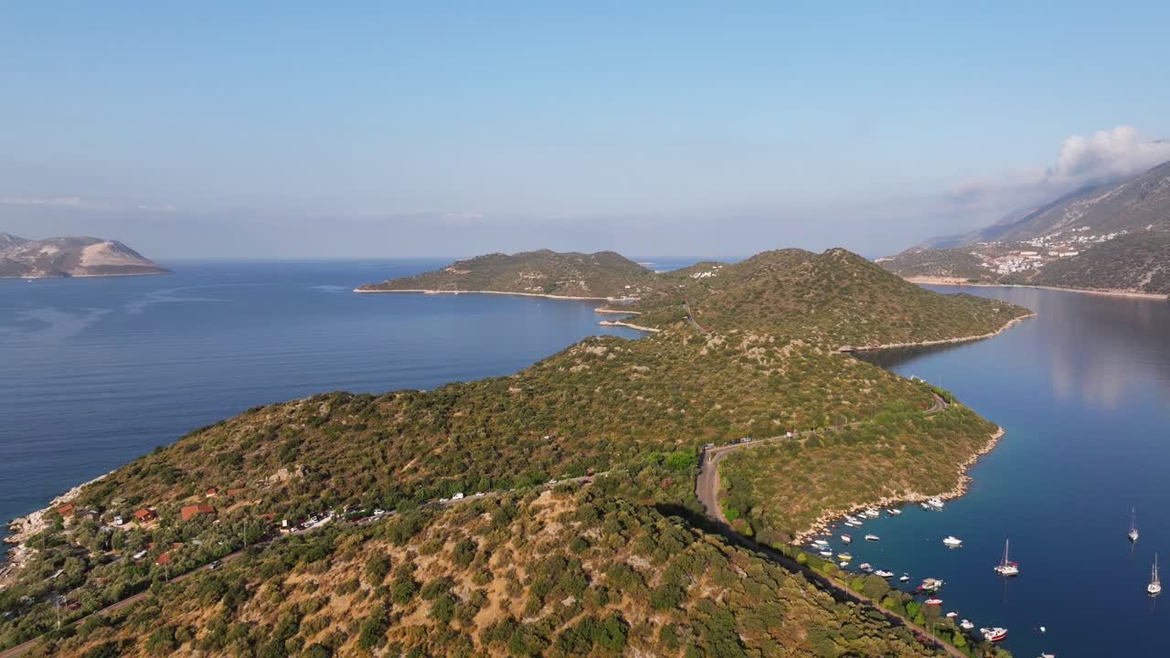 Aerial dolly over the road along Kas coastline in Antalya, Turkey, with boats anchored in the marina and blue waters of the Mediterranean
