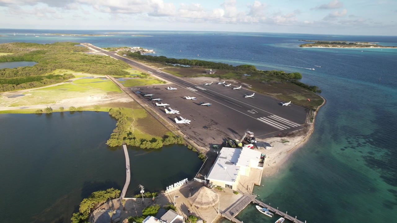 A coastal runway near a lagoon on a sunny day with lush greenery and clear skies, aerial view
