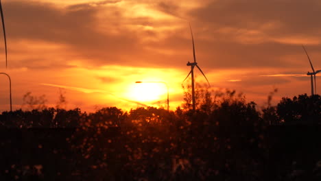 turbinas eólicas al atardecer con el sol poniéndose detrás de ellos, proyectando un resplandor naranja a través del cielo