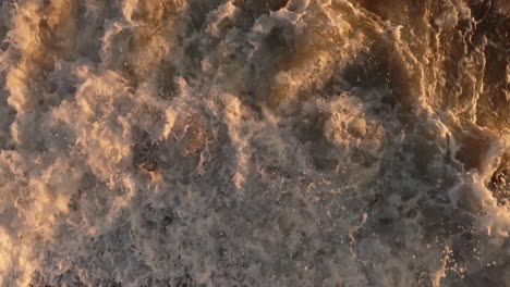 aerial view waves crashing into shore at sunset