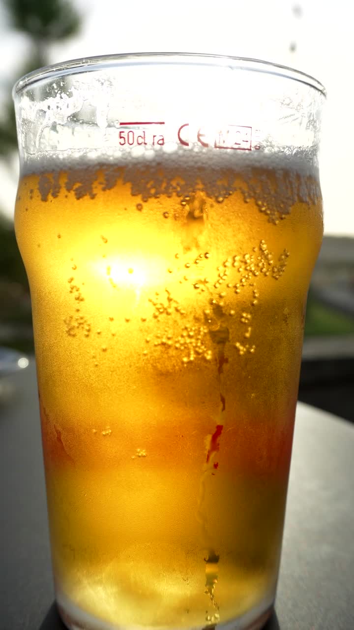 Birra dorata rinfrescante in un bicchiere, retroilluminata dal sole