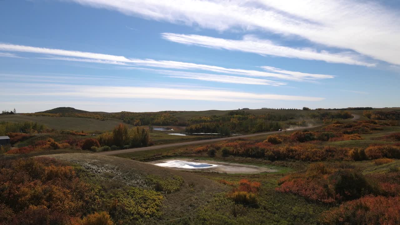 4k drone acercándose a suv conduciendo por un polvoriento camino de tierra durante un soleado día de otoño en el campo de alberta, canadá