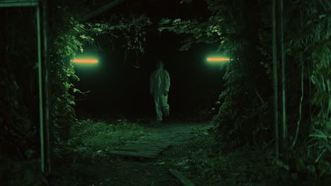person in protective suit walking through a dark forest at night