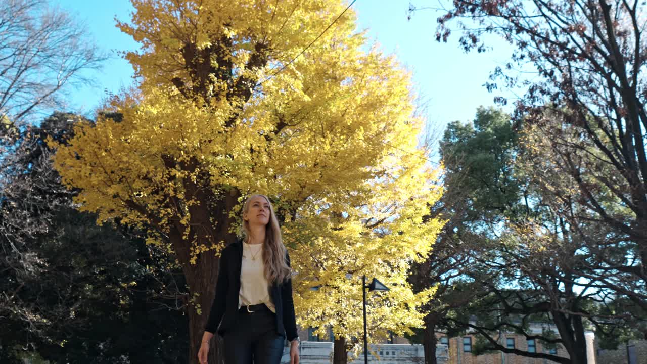 woman strolls peacefully through a serene garden in Tokyo, surrounded by vibrant yellow autumn foliage.