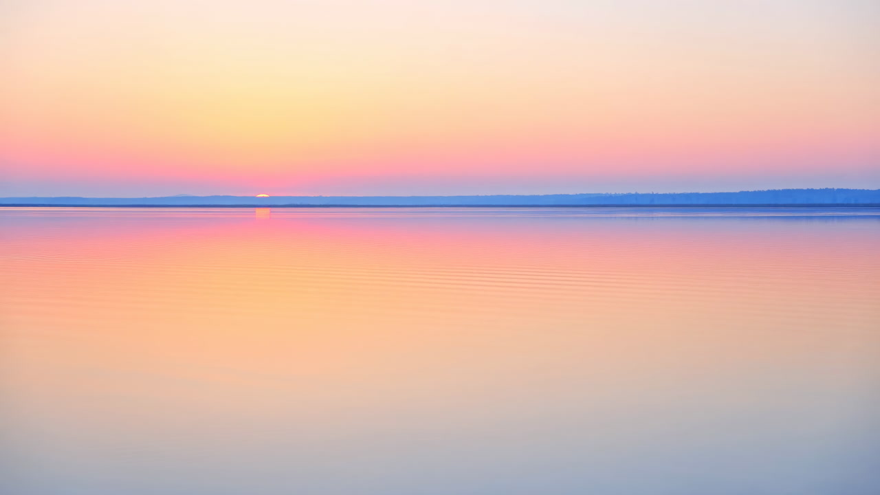 Pastel Sunrise Over Calm Reflective Lake, Glassy Water Mirroring Peach And Lavender Sky, Thin Distant