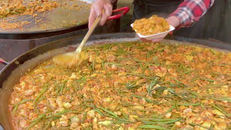 Chicken-and-vegetable-paella-being-served-from-a-large-frying-pan-into-a-plastic-tray-in-an-Edinburgh-street-market,-Edinburgh,-Lothian,-UK