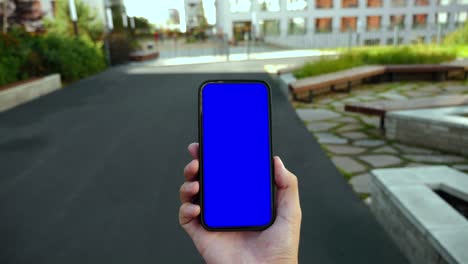 hombre caminando y usando teléfono inteligente pantalla verde croma punto clave de vista. persona caucásica sostener en la mano teléfono modelo y ver programa de video, navegar por internet. ir en teléfono móvil urbano primer plano