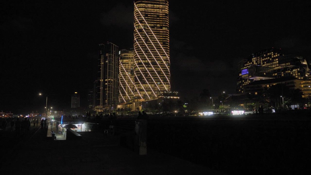Ripresa notturna in tilt-up delle Torri Gemelle ITC Ratnadipa illuminate che si ergono sullo skyline di Colombo, con luci diagonali luminose sulla facciata, lungomare della città e cielo urbano scuro