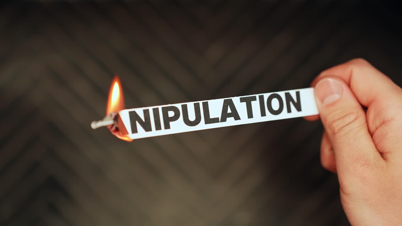 Close-up of a hand holding a paper label reading “MANIPULATION” as the edge burns in flame, symbolizing toxic control, gaslighting, and breaking free