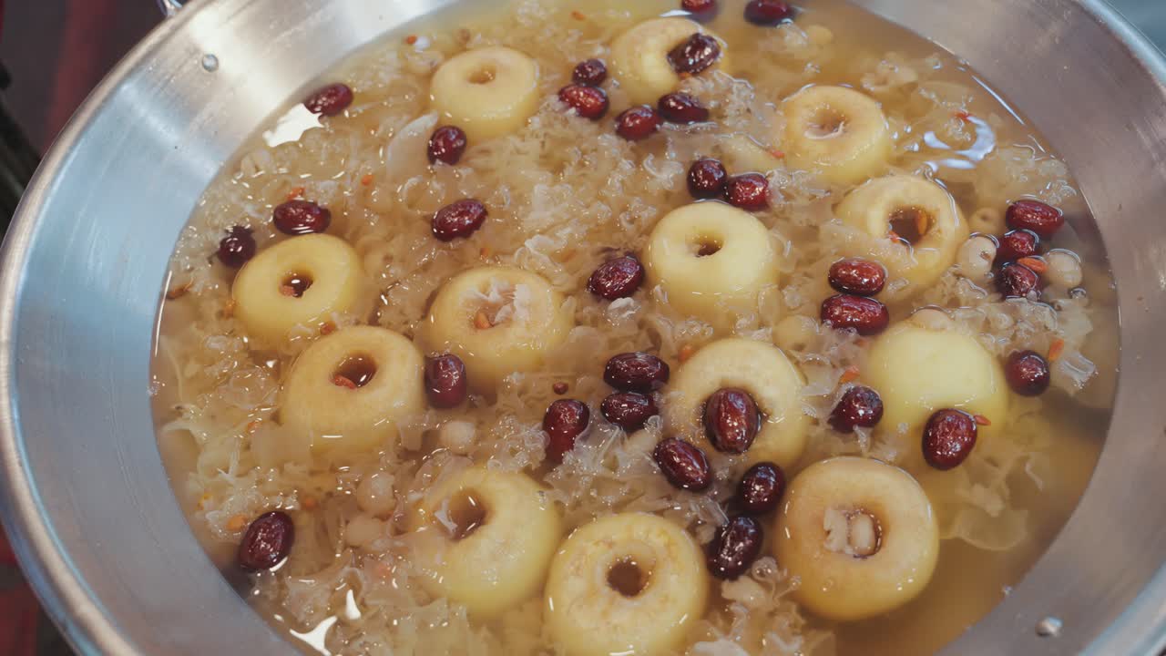 Close-up shot of a traditional Taiwanese sweet soup simmering in a pot, featuring whole pears, red dates, and snow fungus in a gently boiling, aromatic herbal broth