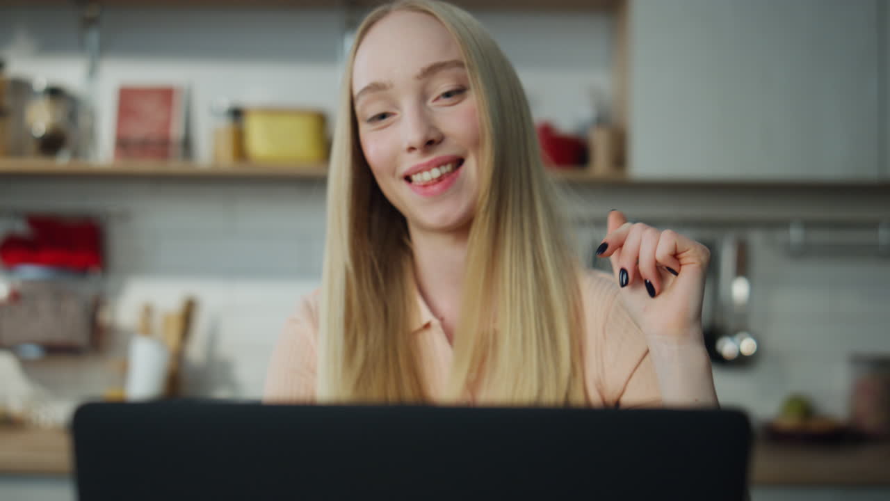 Kobieta czytająca dobre wieści na laptopie, siedząca w kuchni, zbliżenie. Dziewczyna patrząca na ekran.