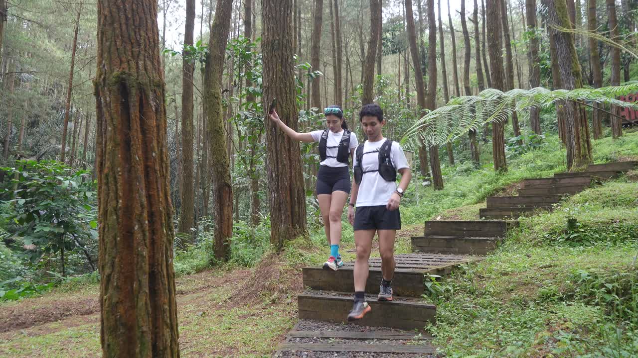 Indonesian couple on forest trail run with woman recording video on smartphone