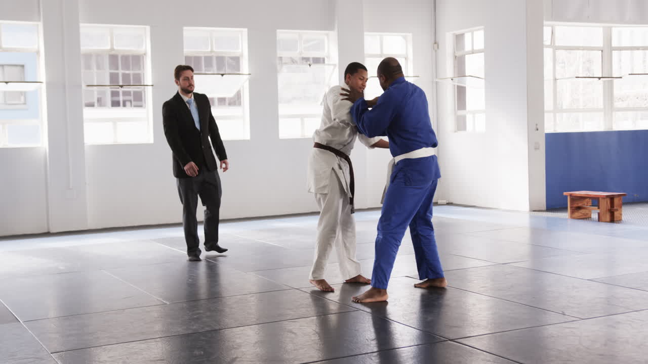 Judo practitioners sparring intensely in dojo under instructor's watchful eye