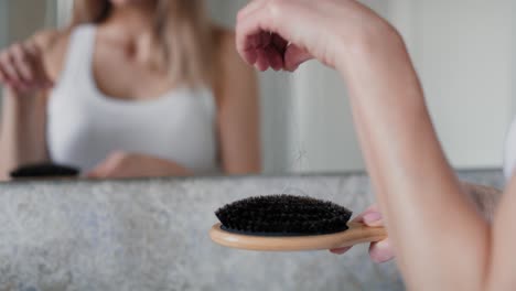 caucasian woman brushing hair in the bathroom and looking at their loss on the brush.