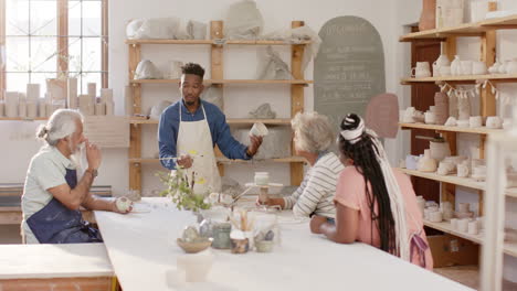 happy diverse group of potters glazing clay jugs and discussing in pottery studio