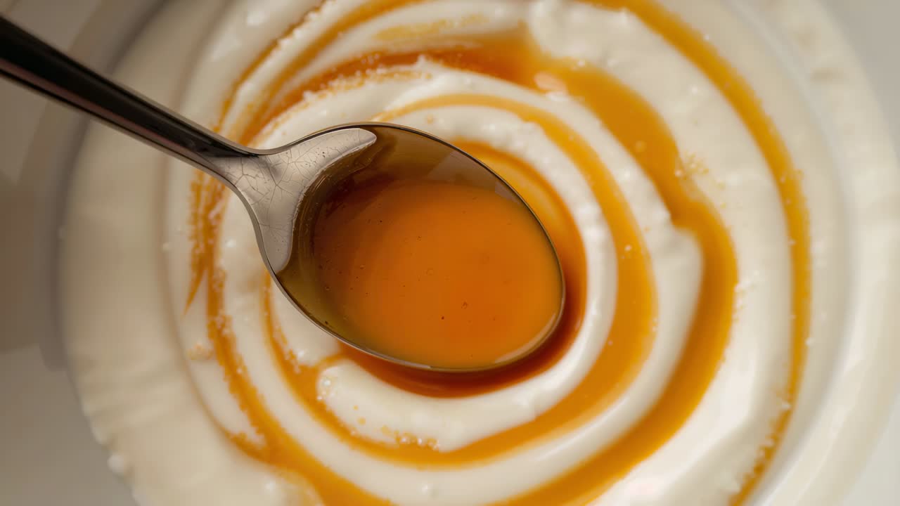 Lett berøring av krem, roterende metallskje som tegner en ravfarget saus som danner en spiral i en bolle på benken