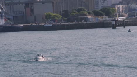 small fishing boat leaving cherbourg harbour in northern france with tourists people standing on waters edge. slow motion footage 4k.