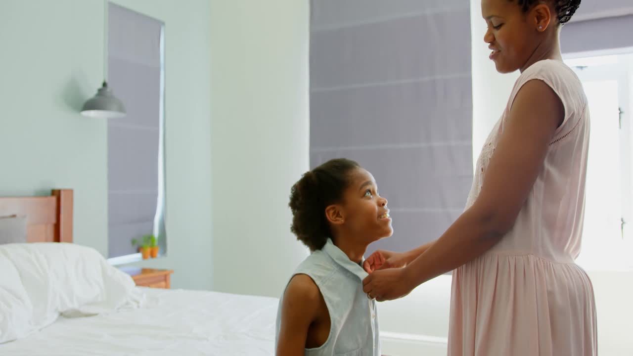 Side view of mid adult black mother helping her daughter in wearing dress in a comfortable home 4k