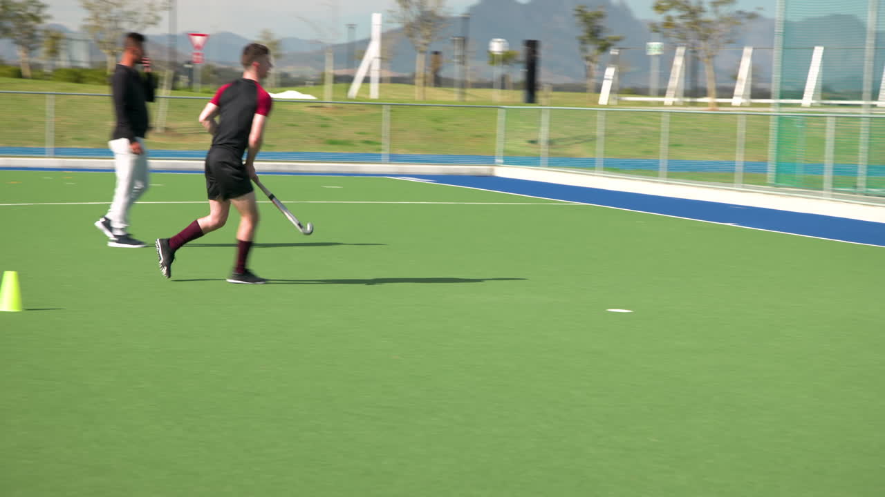 Playing field hockey, two men practicing on outdoor sports field, sunny day