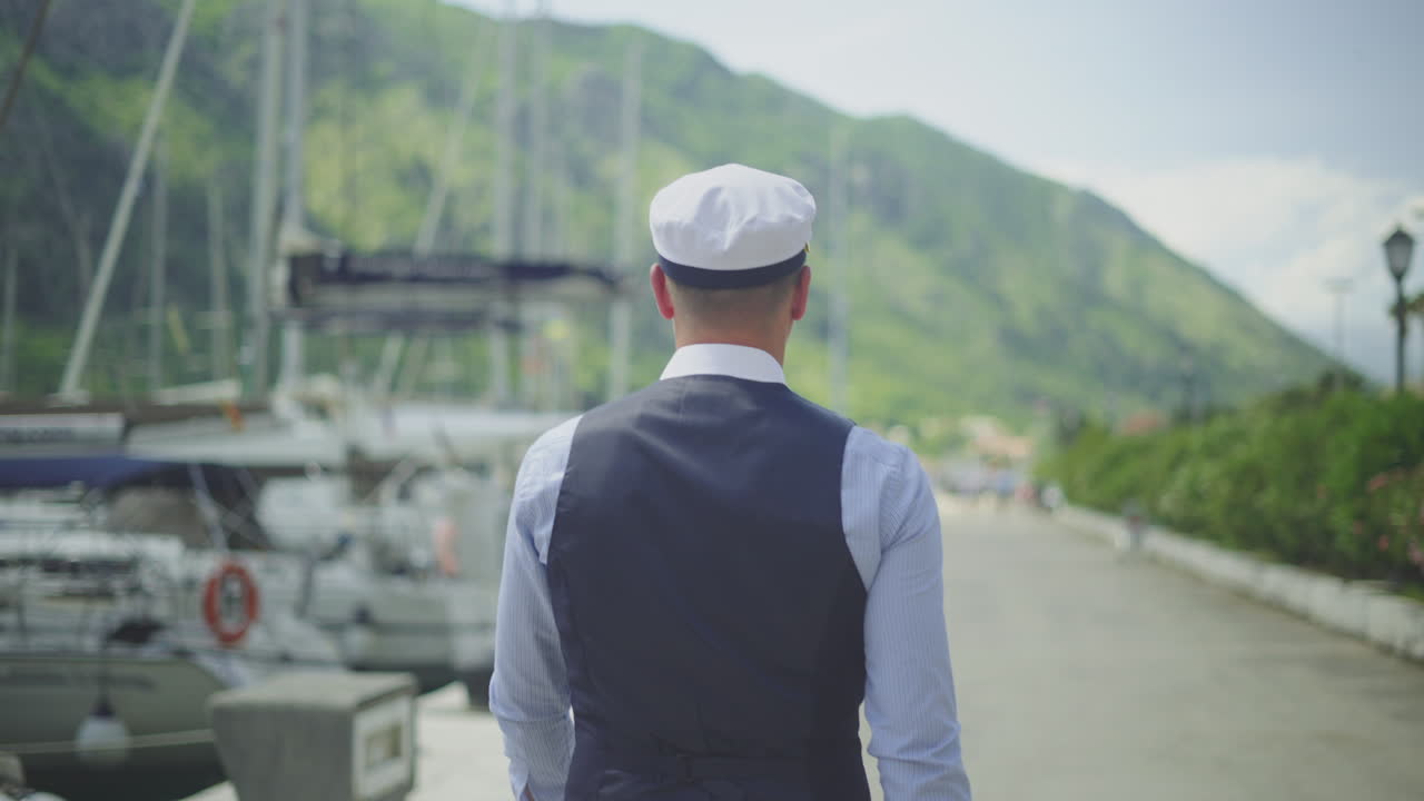 Man in Captain's Hat Walking on a Waterfront Pier