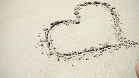 girl draws a heart on the sea sand. the waves wash away the heart drawn on the sand.