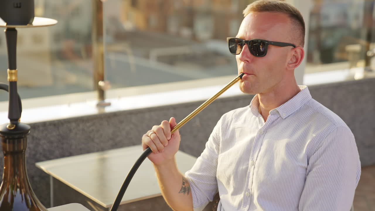 Young man having relaxing time resting in hookah bar. Male in sunglasses smoking shisha close up. Blurred backdrop.