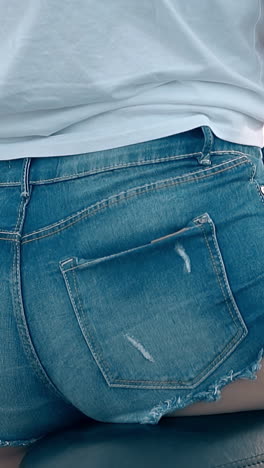 slow motion girl in t-shirt and denim shorts sits on motorcycle holding man shoulders close backside view