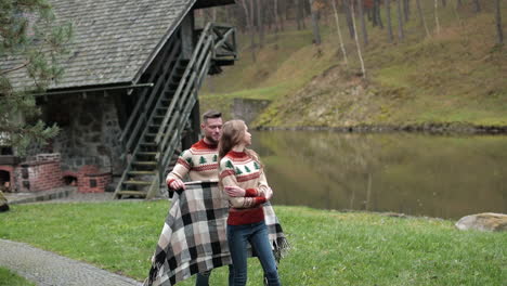 caring boyfriend brings checkered plaid to his girlfriend. young couple hugging near the river in the countryside. beautiful couple in the autumn village.