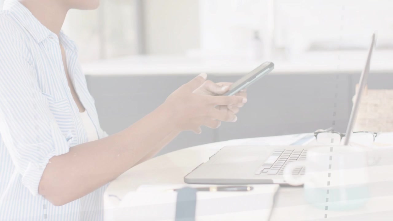 Donna al bancone che prende lo smartphone, toccando lo schermo mentre passa dal laptop per un'attività lavorativa