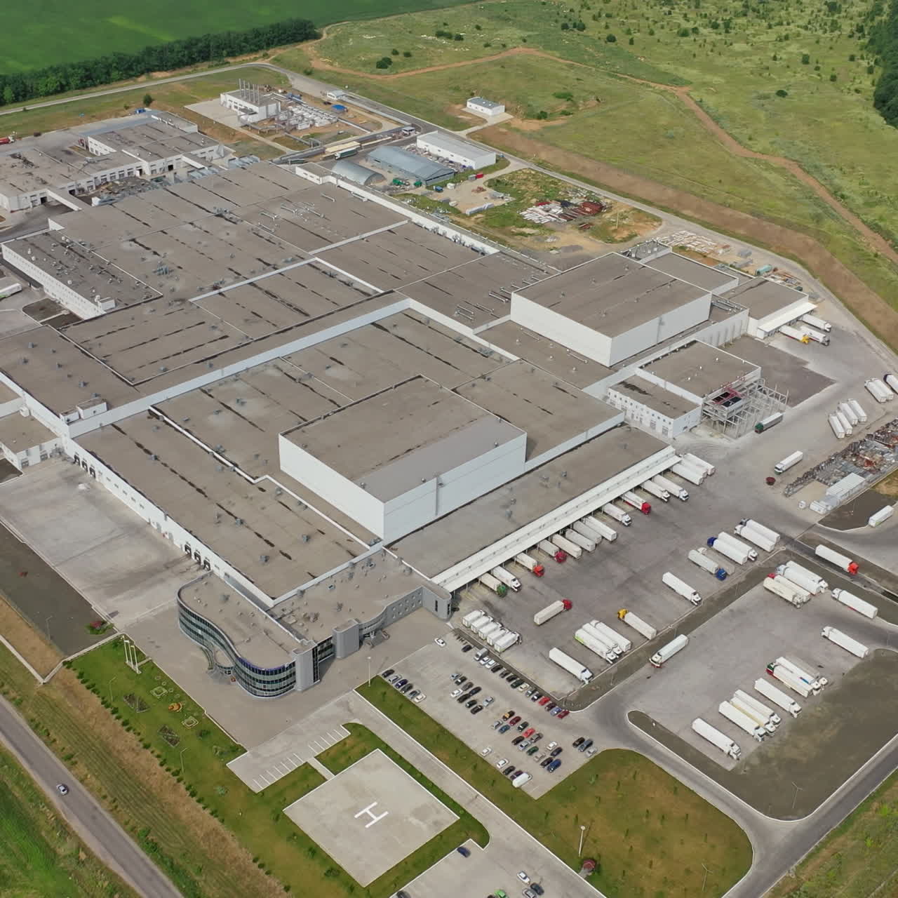 Top view of a large industrial center with parking for trucks. Aerial view on the modern manufacturing complex surrounded by nature. Slow motion camera.