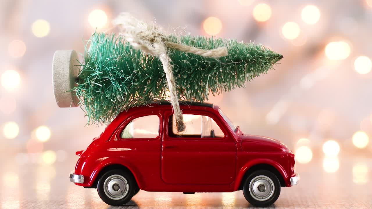 Macchinina rossa con albero di Natale sul tetto e luci intermittenti sullo sfondo.