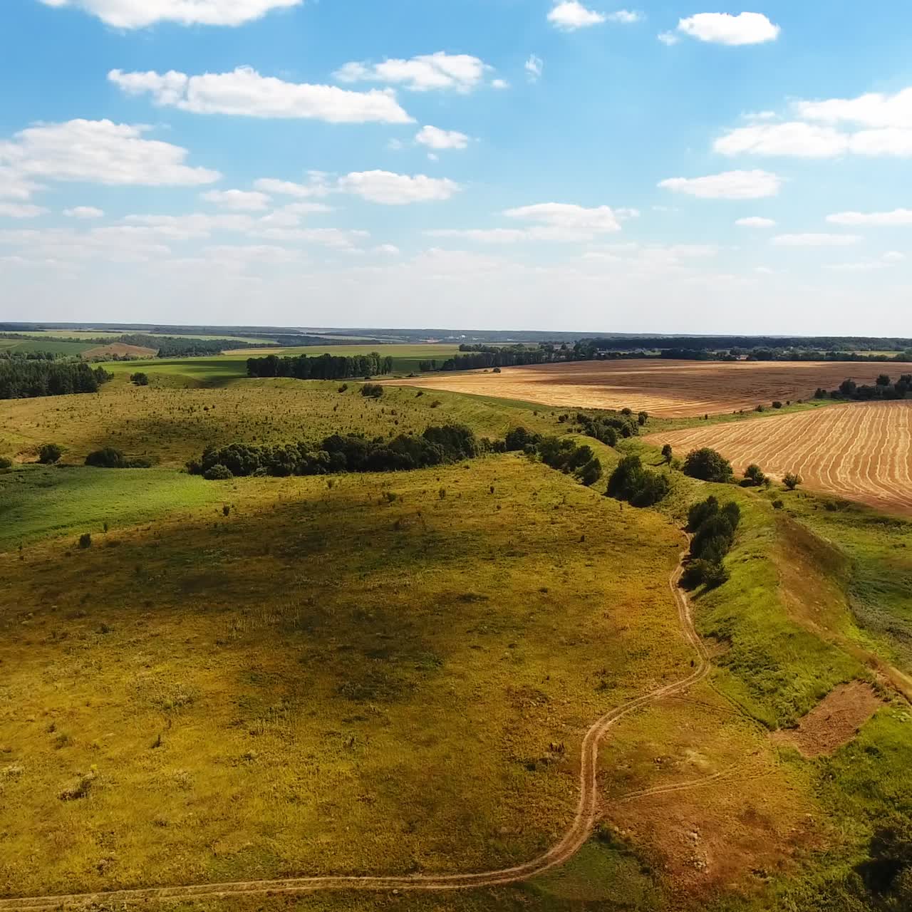 Green meadows, river, forests and wheat farmlands against blue sky. Shadows from clouds cover the ground