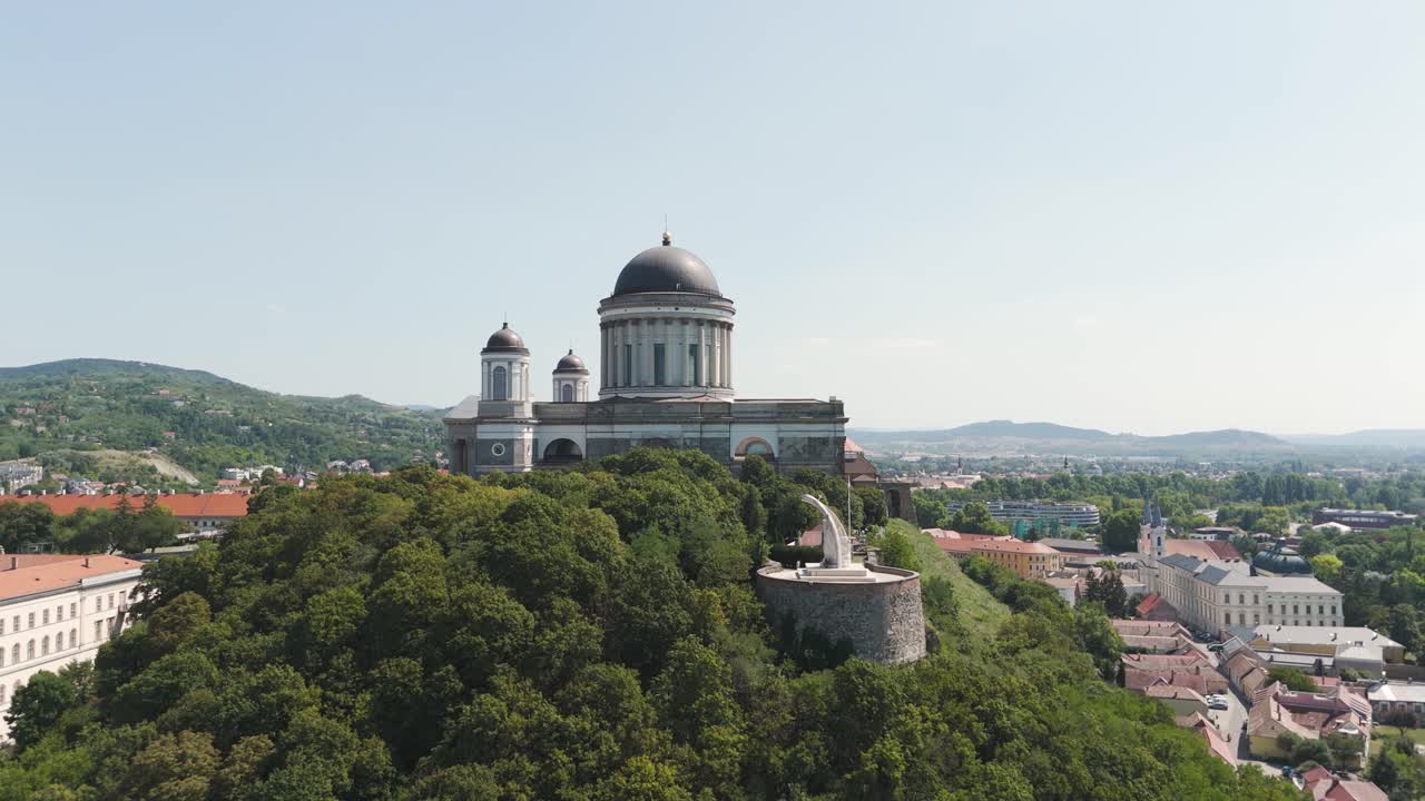 Aerial view of the Esztergom Basilica, a beautiful landmark in Hungary, surrounded by lush greenery. Pull Back Shot