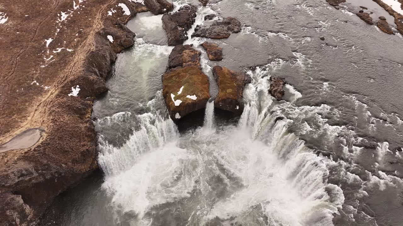 Overhead drone view of Goðafoss waterfall in Iceland, showing powerful water flow over rocky formations