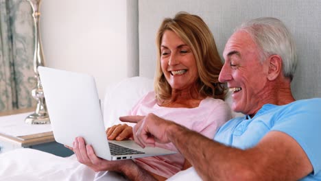 happy senior couple on bed using laptop