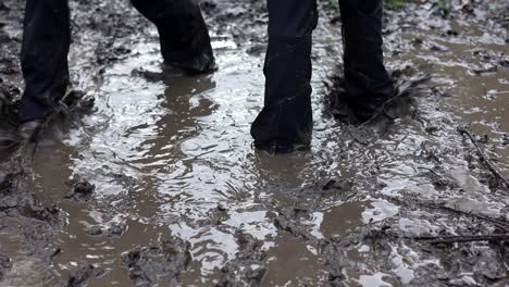 two young children splashing in a muddy puddle, wearing waterproof clothing