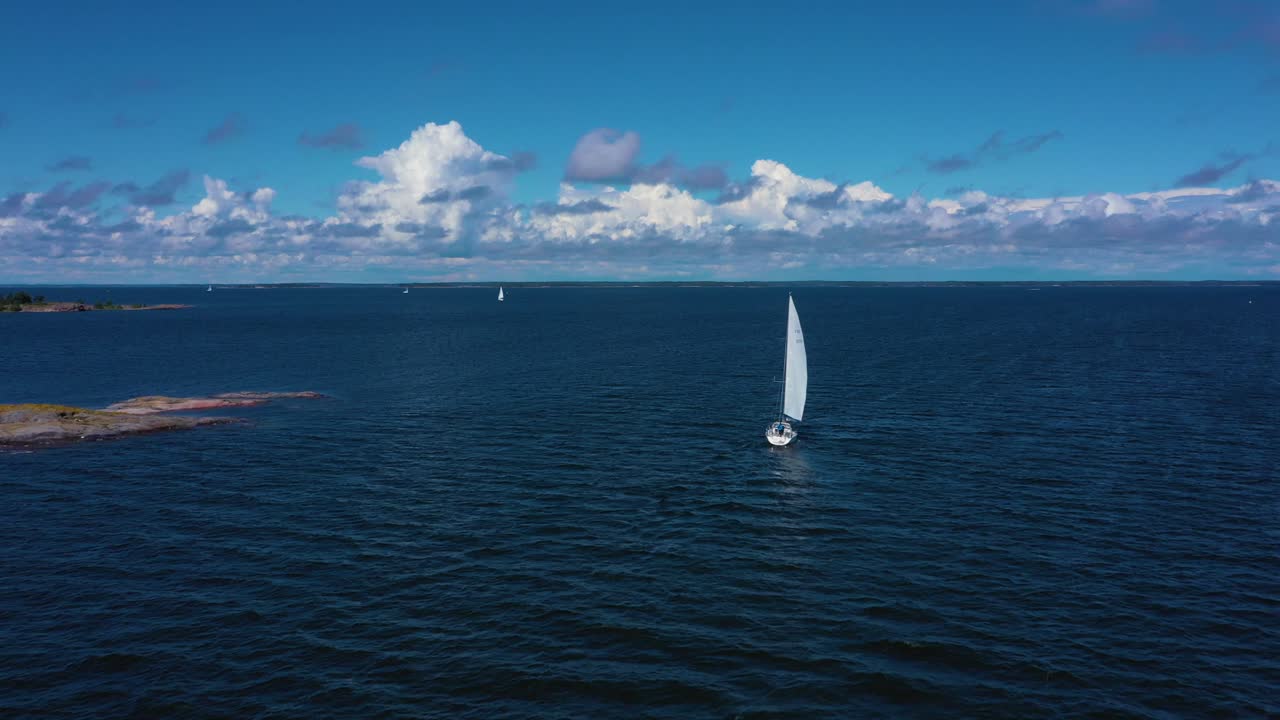 Aerial view of a white sailboat on the open sea, at the Gulf of Finland, bright, sunny, summer day, in Uusimaa, Finland - low, dolly, drone shot