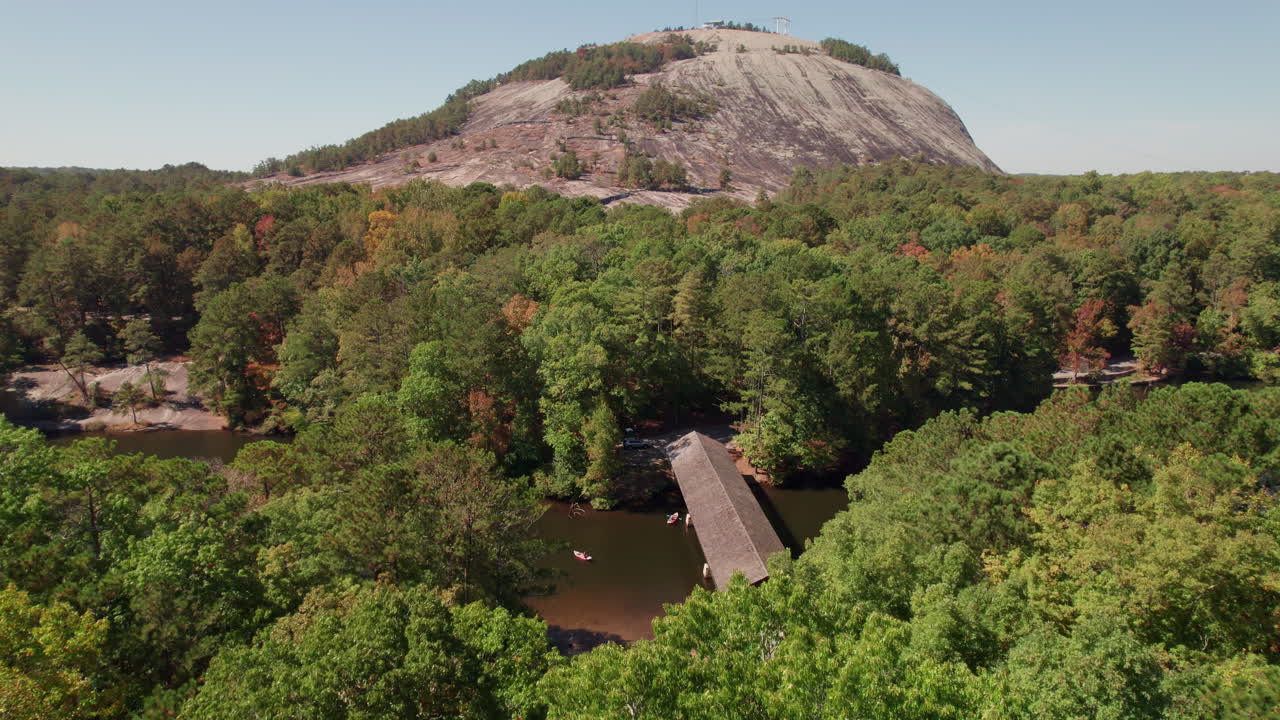 A cinematic aerial flyover the lush tree canopy and river approaching Stone Mountain in the popular state park for hiking, tourism, kayaking, cycling, and outdoor recreation in Georgia.