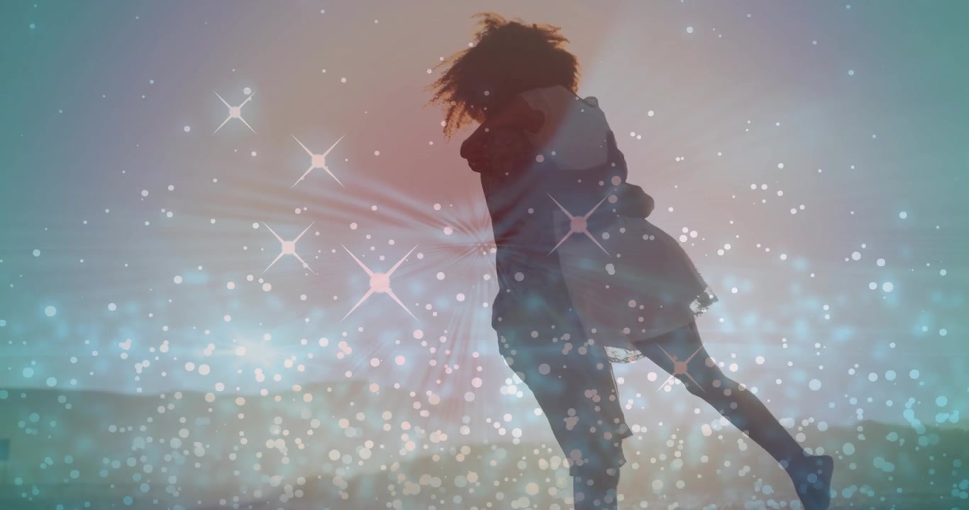 Uomo che si china per sollevare una donna, la porta in braccio ruotando sulla riva, con un effetto glitter che si attenua per una pubblicità aziendale.
