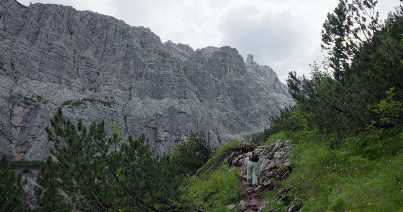 İtalya, Veneto, Dolomitler'deki Lago di Sorapis yakınlarındaki patika boyunca yürüyen, Alp dağları ve kayalık araziyle çevrili bir kadın yürüyüşçü - geniş çekim.