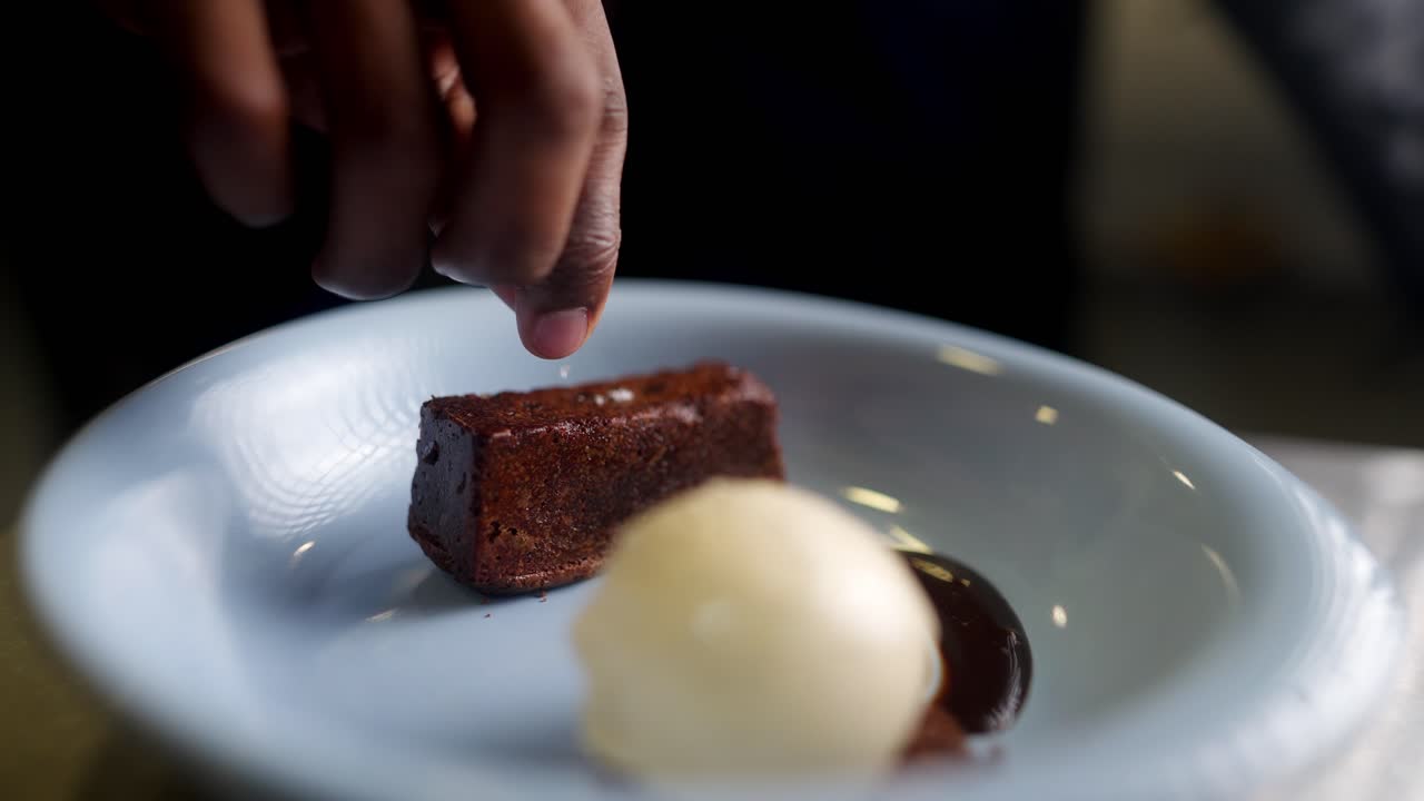 Close up view in slow motion of a Pastry chef adding coarse salt to a chocolate brownie and vanilla ice cream dessert under cinematic and beautiful atmosphere.